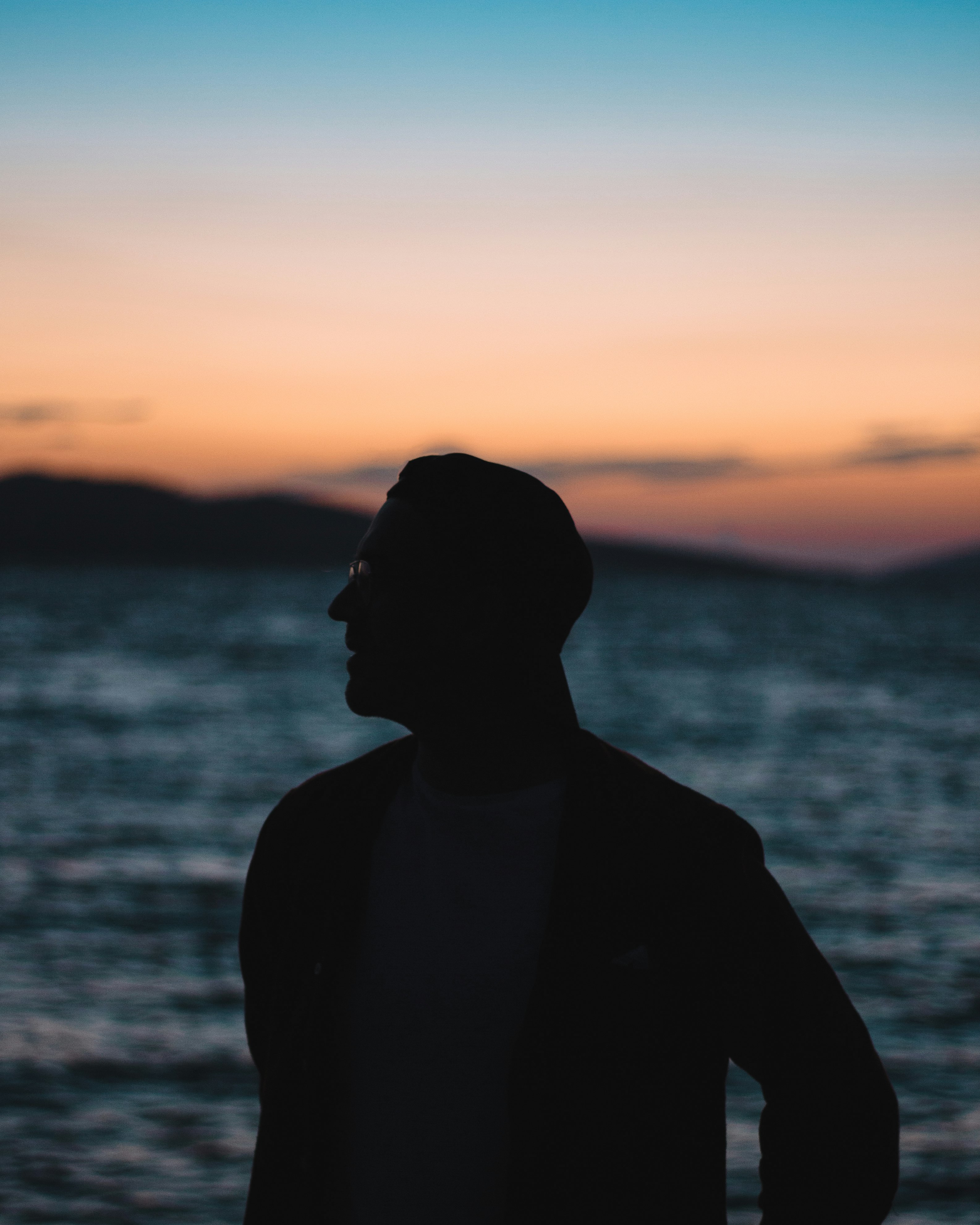 silhouette of man standing near body of water during sunset